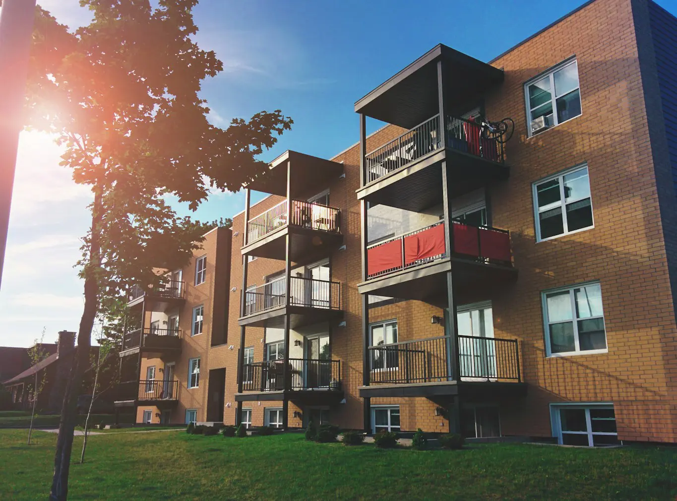 A multi-story brick apartment building with several levels of balconies under a sunny sky.