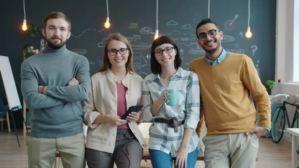 Four colleagues posing together in an office with a chalkboard wall in the background.